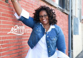 A woman leaning against a brick wall with her arm up.